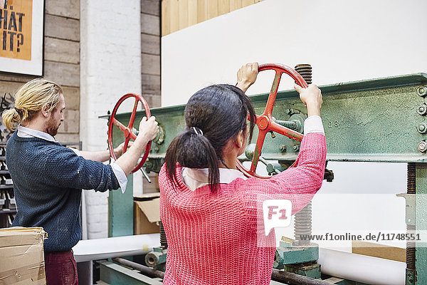 Mann und Frau drehen Druckmaschinenräder in traditioneller Druckwerkstatt