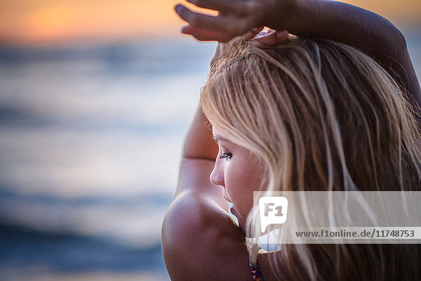 Young woman with arms raised on beach at sunset