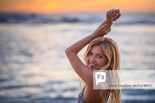 Portrait of young woman with arms raised on beach at sunset