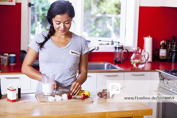 Young woman slicing strawberry in kitchen