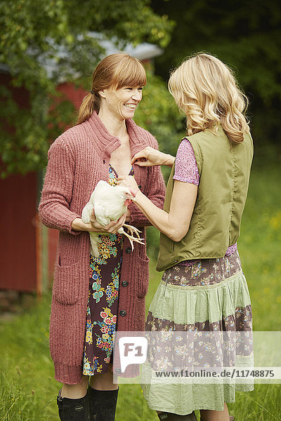 Two women in field holding hen