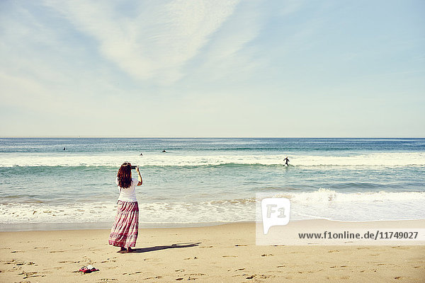 Rückansicht einer Frau am Strand beim Fotografieren des Ozeans  Venice Beach  Los Angeles  Kalifornien