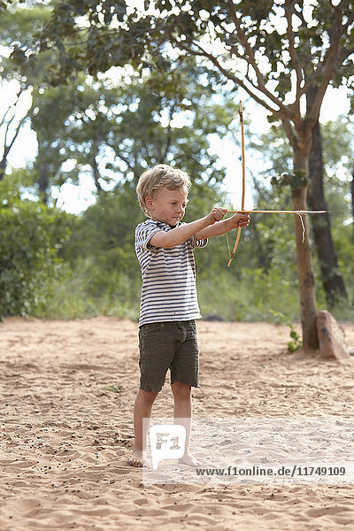 Young boy on sand holding home-made bow and arrow