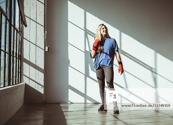 Frontansicht einer jungen Frau in Turnhalle in Sportkleidung in voller Länge  die lächelnd wegschaut