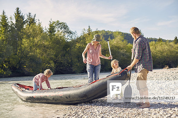 Familie zieht Beiboot auf Flussufer  hält Paddelbretter