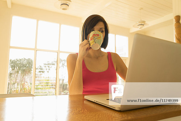 Geschäftsfrau trinkt Tablette beim Laptop-Lesen im Wohnzimmer