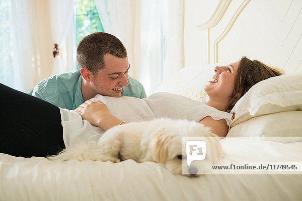 Pregnant woman and partner lying on bed with dog