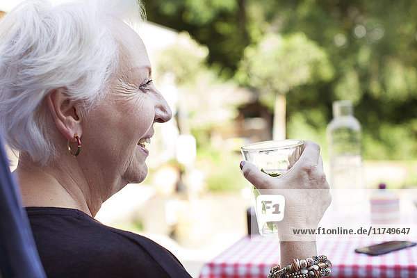 Ältere Frau entspannt sich im Garten  hält kaltes Getränk