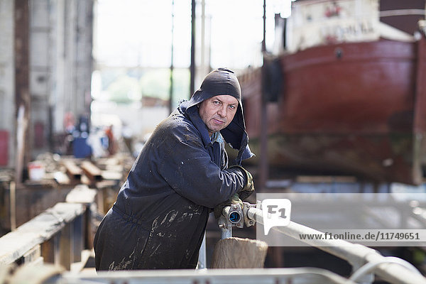 Portrait of worker leaning against railings in shipyard workshop