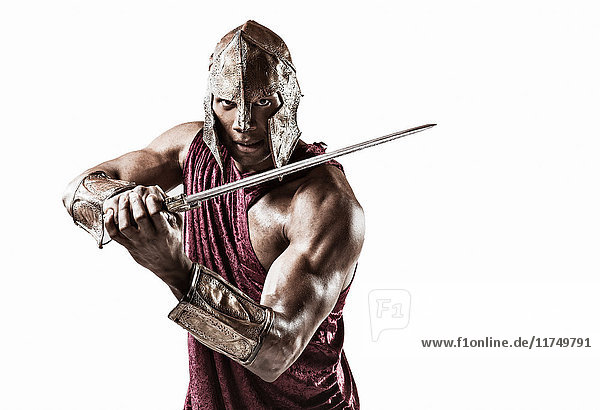 Studioporträt eines muskulösen jungen Mannes als Gladiator verkleidet mit Helm und Schwert