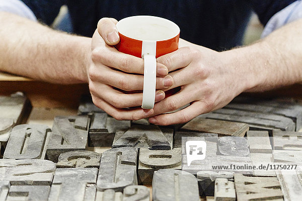 Nahaufnahme der Hände junger Männer beim Kaffeetrinken in der traditionellen Druckwerkstatt