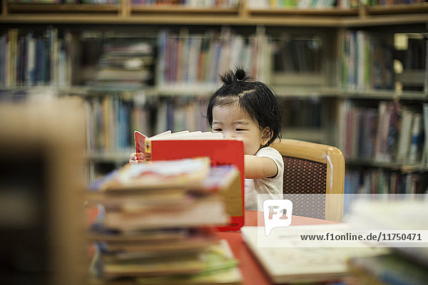 Ein Jahr altes Mädchen liest Buch in der Bibliothek