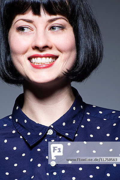 Young woman in blue spotted blouse looking away smiling