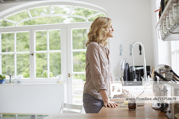 Mittlere erwachsene Frau  die an der Küchentheke steht und aus dem Fenster schaut