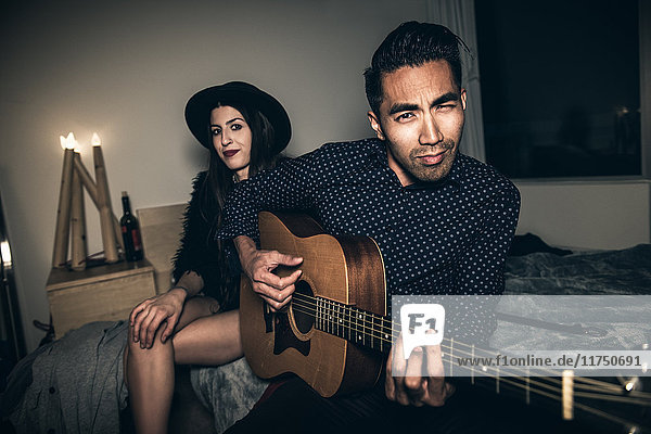 Junges Paar sitzt auf dem Bett  junger Mann spielt Gitarre