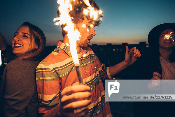 Eine Gruppe von Freunden genießt eine Dachparty und hält brennende Wunderkerzen