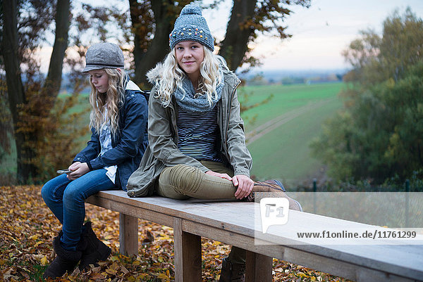 Porträt eines Mädchens und ihrer Schwester auf einer herbstlichen Parkbank sitzend