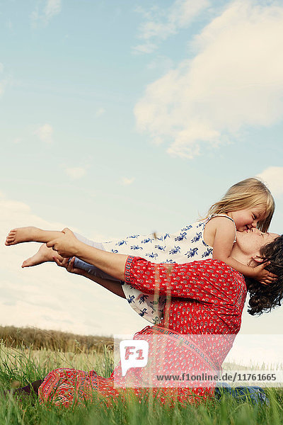 Pregnant woman sitting in field kissing toddler daughter