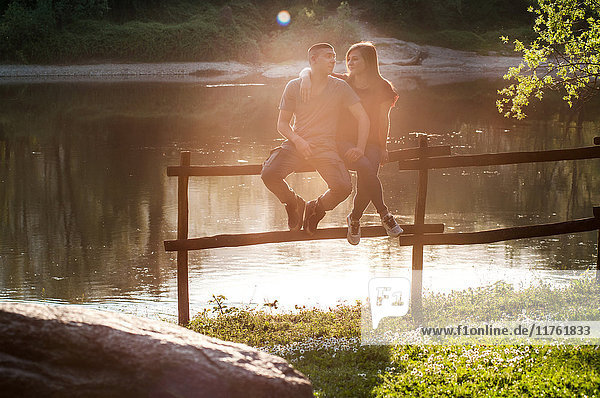 Ehepaar sitzt auf einem Zaun am Fluss  zufriedene Mienen