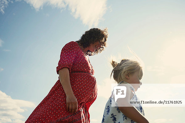 Weibliches Kleinkind schlendert mit der Mutter gegen den blauen Himmel