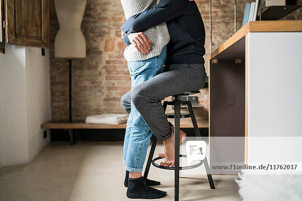 Junger Mann umarmt Freundin vom Küchenhocker