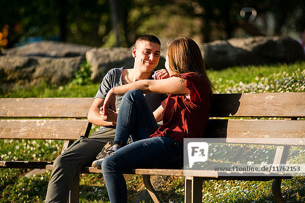 Couple sitting on park bench  face to face  smiling