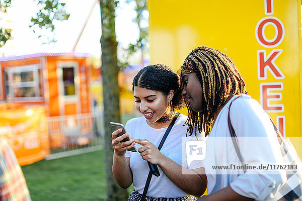 Two girls at funfair  looking at smartphone