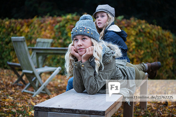 Porträt eines blonden Mädchens und ihrer Schwester auf einer Gartenbank im Herbst