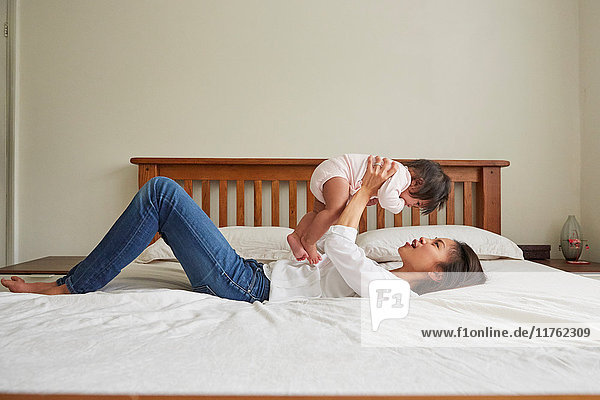 Woman lying on bed holding up baby daughter