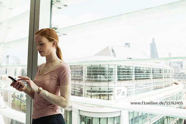 Businesswoman using mobile phone by office window  London  UK