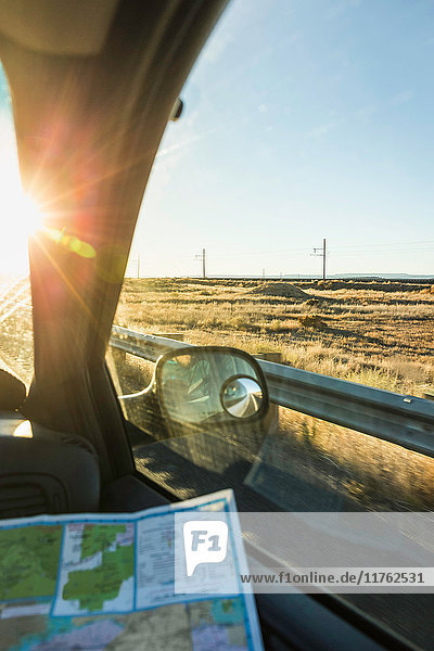 Wing mirror view of man with map on the road in sunlight Arizona USA