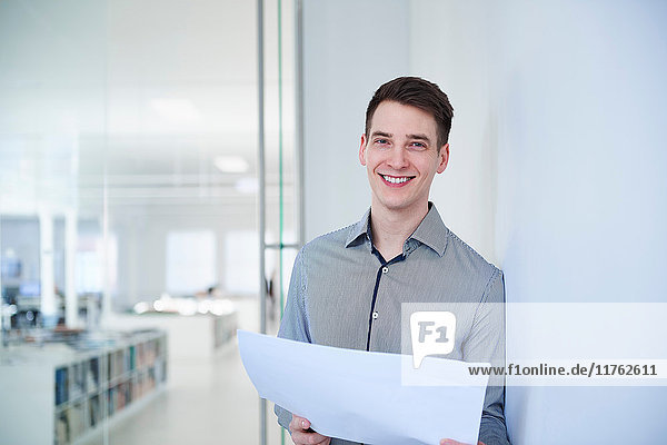 Porträt eines Architekten im Büro  der Blaupausen hält und lächelnd in die Kamera schaut