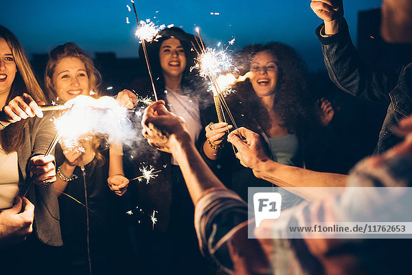 Group of friends enjoying roof party  holding lit sparklers