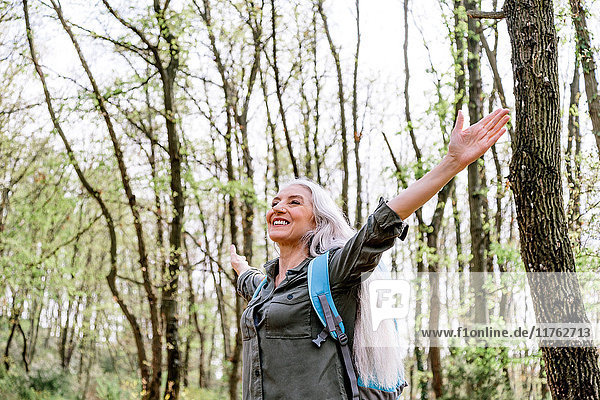 Reife Frau mit langen grauen Haaren mit offenen Armen im Wald  Scandicci  Toskana  Italien