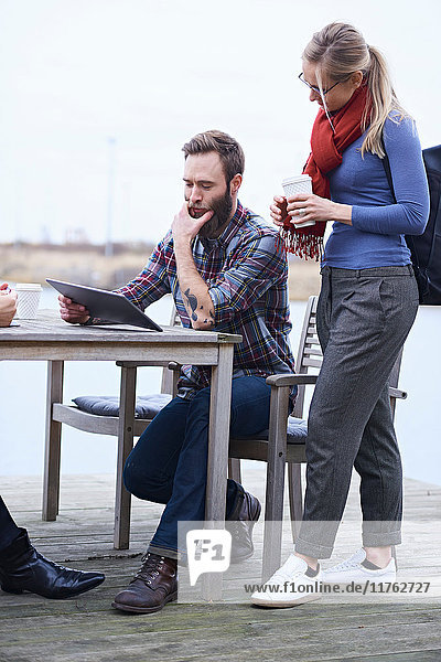 Männliches und weibliches Designteam betrachtet digitales Tablett am Wasser vor dem Designstudio