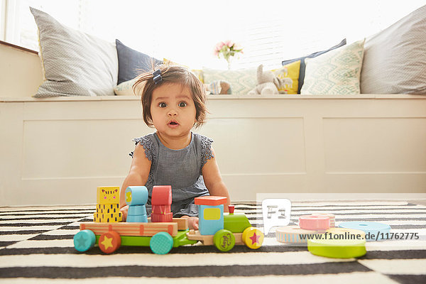 Porträt eines auf einem Teppich sitzenden Mädchens  das mit einer Spielzeugeisenbahn spielt