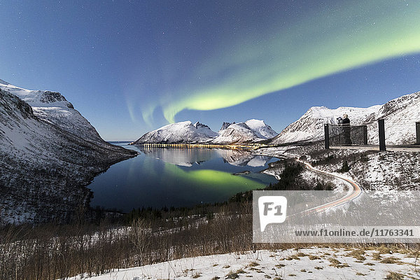 Fotograf auf Plattform bewundert das Nordlicht (Aurora Borealis) und die Sterne  die sich im kalten Meer spiegeln  Bergsbotn  Senja  Troms  Norwegen  Skandinavien  Europa