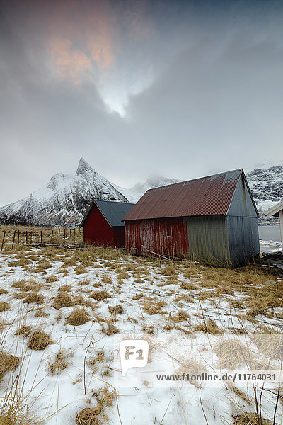 Wolken auf schneebedeckten Gipfeln über einer typischen Holzhütte namens Rorbu  Senja  Ersfjord  Provinz Troms  Norwegen  Skandinavien  Europa