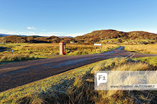 Ein herbstlicher Blick auf eine rote Telefonzelle am Rande einer ruhigen Straße in den abgelegenen Ardnamurchan-Mooren der schottischen Highlands  Schottland  Vereinigtes Königreich  Europa