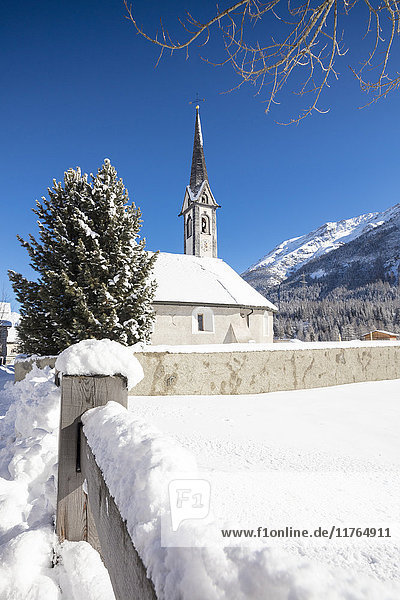 Schneebedeckte Alpenkirche  umrahmt von blauem Himmel  Cinuos  Kanton Graubünden  Engadin  Schweiz  Europa