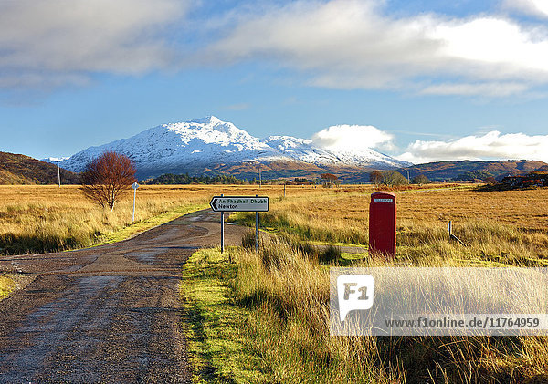 Winteransicht einer roten Telefonzelle und einer Straße in Richtung des schneebedeckten Berges Beinn Resipol in den Mooren der schottischen Highlands  Schottland  Vereinigtes Königreich  Europa