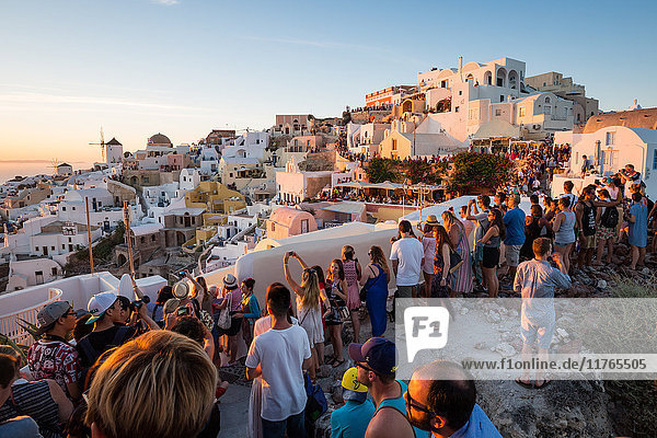 Menschen säumen die Stadtmauern  um den berühmten Sonnenuntergang in Oia auf der griechischen Insel Santorin zu erleben  Kykladen  Griechische Inseln  Griechenland  Europa