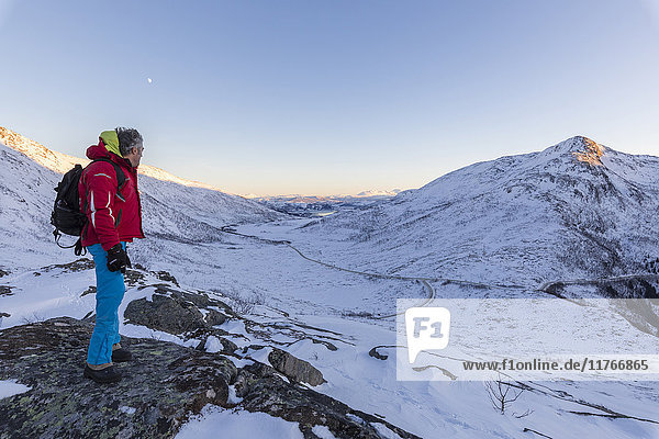 Hiker on top of the rocky crest admires the snowy peaks of Fjordbotn Lysnes Senja Troms Norway Scandinavia Europe