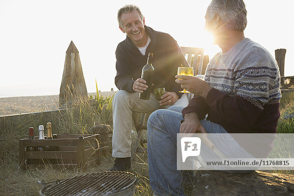 Senioren trinken Wein und grillen am Strand bei Sonnenuntergang
