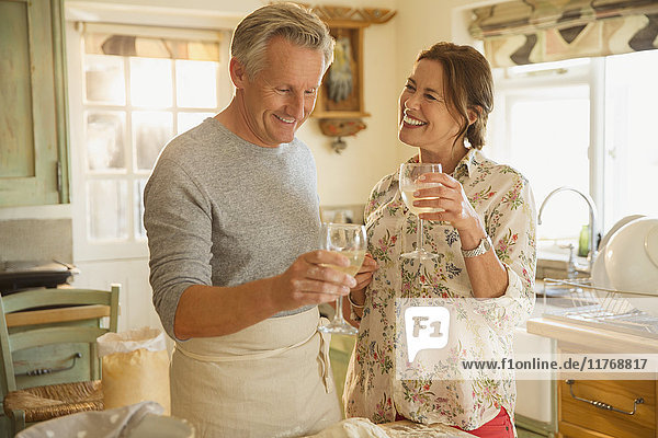 Smiling mature couple drinking wine and cooking in kitchen