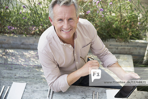 Portrait lächelnder älterer Mann mit digitalem Tablett auf der Terrasse