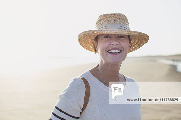 Portrait lächelnde reife Frau mit Strohhut am sonnigen Sommerstrand