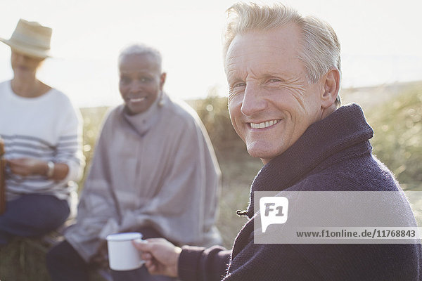 Portrait lächelnder älterer Mann beim Kaffeetrinken mit Freunden am sonnigen Strand