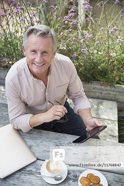 Portrait lächelnder älterer Mann mit digitaler Tablette und Kaffeetrinken am Terrassentisch