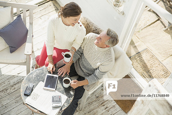 Blick von oben auf ein reifes Paar  das Kaffee trinkt und ein digitales Tablett auf der Sonnenterrasse benutzt.